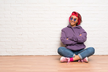 Young woman with pink hair sitting on the floor with glasses and smiling