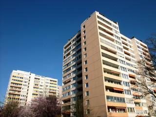 Hochhaussiedlung mit Mietwohnungen in hellen Pastelltönen und Naturfarben vor blauem Himmel im...