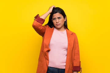 Young Colombian girl over yellow wall having doubts while scratching head