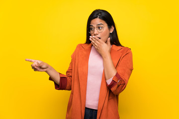 Young Colombian girl over yellow wall pointing finger to the side with a surprised face