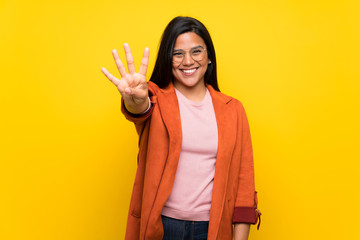 Young Colombian girl over yellow wall happy and counting four with fingers