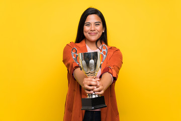 Young Colombian girl over yellow wall holding a trophy