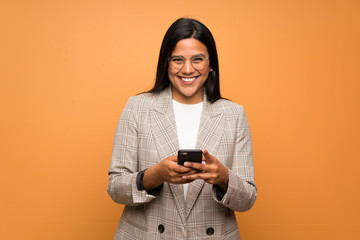 Young Colombian girl over brown wall sending a message with the mobile