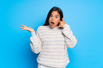 Fototapeta premium Young Colombian girl with sweater surprised and making phone gesture