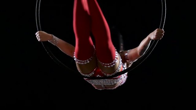 Gymnast spinning in the air on a hoop with a low head. Black smoke background. Slow motion. Close up