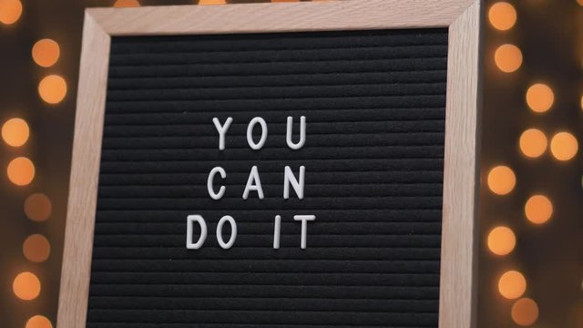 Black letter board with YOU CAN DO IT title on it. Camera rotating around the sign showing the beautiful bokeh balls in the background.