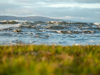 Dramatic ocean's waves in focus, grass in foreground out of focus. Mountains in the background. Galway bay.
