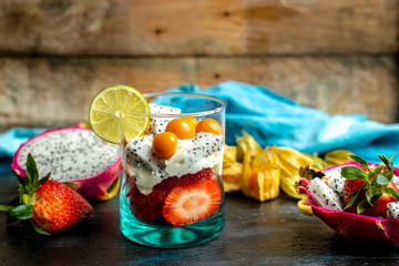 fresh fruit of strawberries, among them beautiful, pink dragon fruit, next to the dessert made of his pulp, whipped cream, lime, physalis and pieces of strawberry