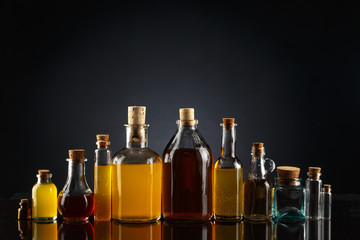 Glass bottles of different shapes and sizes filled with liquids of different colors on a black background.