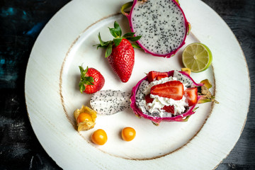 on a white, wooden plate, lie the fresh fruit of strawberries, among them a beautiful, pink dragon...