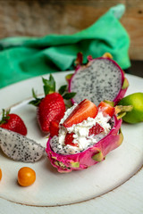 fresh fruit of strawberries, among them beautiful, pink dragon fruit, next to the dessert made of his pulp, whipped cream, lime, physalis and pieces of strawberry