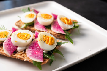Colorful sandwiches of cereal bread with boiled eggs with radish and arugula