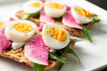 Colorful sandwiches of cereal bread with boiled eggs with radish and arugula
