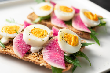 Colorful sandwiches of cereal bread with boiled eggs with radish and arugula