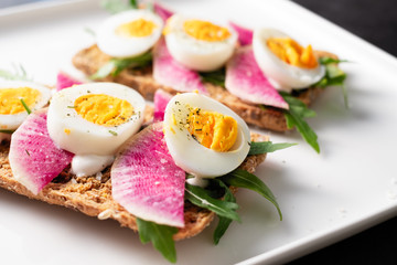 Colorful sandwiches of cereal bread with boiled eggs with radish and arugula