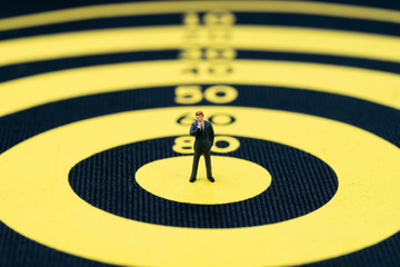 Business goal, target and achievement or leadership concept, miniature people small brave confident businessman figurine standing at the center of yellow and black dartboard with score number
