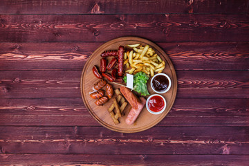 Sausage set for beer. Sausage, french fries, crackers, ketchup and sauce on the cutting board and wooden background.