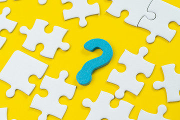 Asking question and answer for business solution, creativity or teamwork concept, blue wooden question mark symbol with white jigsaw puzzle on solid yellow background