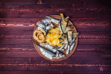 Snacks for beer. Salted, dried fish, squid rings and potato chips, on the cutting board and wooden background
