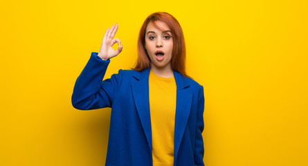 Young redhead woman with trench coat surprised and showing ok sign