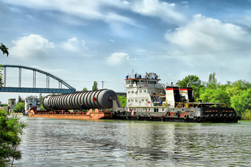 Heavy oversized chemical apparatus is transported by river transport through the shipping channel on a special barge - obrazy, fototapety, plakaty