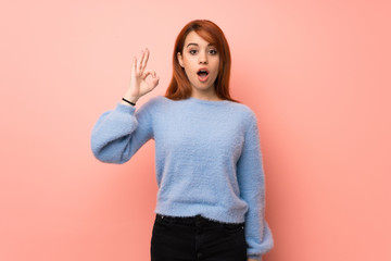 Young redhead woman over pink background surprised and showing ok sign