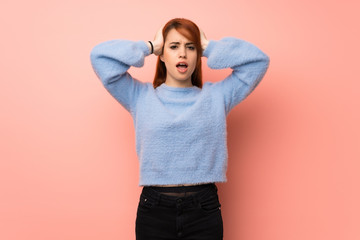 Fototapeta na wymiar Young redhead woman over pink background takes hands on head because has migraine