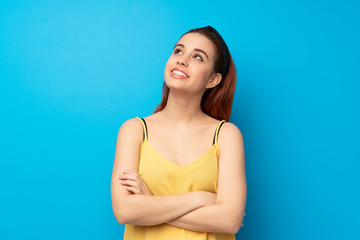 Young redhead woman over blue background looking up while smiling
