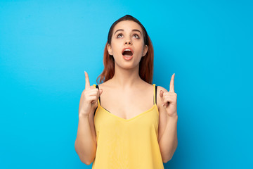 Young redhead woman over blue background surprised and pointing up