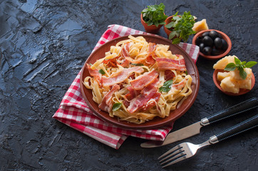 Classic pasta Carbonara, with bacon, egg, Parmesan cheese and Basil on a black slate background. Pieces of Parmesan, Basil, spices, olives and a fork lie near on the table. Copy space