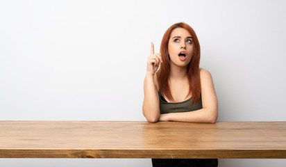 Fototapeta na wymiar Young redhead woman at desk thinking an idea pointing the finger up