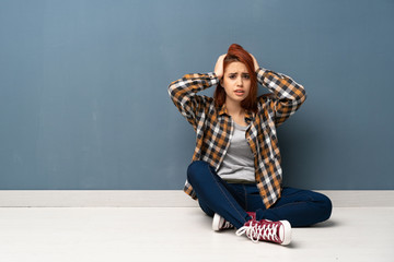 Young redhead woman sitting on floor frustrated and takes hands on head