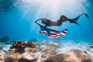 Woman freediver swim over sandy sea bottom with USA flag. Independence day