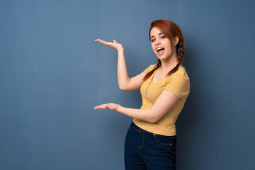Young redhead woman over blue background extending hands to the side for inviting to come