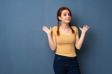Young redhead woman over blue background making unimportant gesture while lifting the shoulders