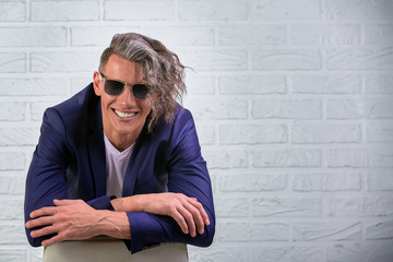 stylish businessman with curly long hair in sunglasses sitting on chair on white background