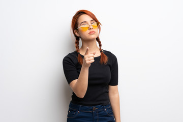 Young redhead woman over white wall frustrated and pointing to the front