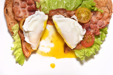 Sandwich with fried bacon and cherry tomatoes. Sliced fried egg and spilled yolk. Unhealthy food for breakfast. Close-up