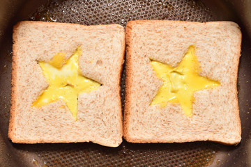 Roasting bread toasts with a star-shaped middle and omelette filled with egg to create a sandwich. Bread is fried for sandwiches in a pan with a non-stick coating, close-up