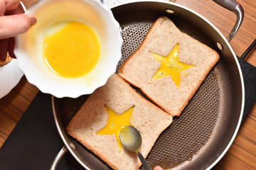Roasting bread toasts with a star-shaped middle and a girl's hand fills it with a beaten egg to create a sandwich. Bread is fried for sandwiches in a pan with a non-stick coating, close-up