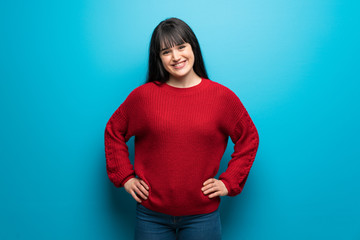 Obraz na płótnie Canvas Woman with red sweater over blue wall posing with arms at hip and smiling