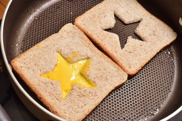 Roasting bread toasts with a star-shaped middle and omelette filled with egg to create a sandwich. Bread is fried for sandwiches in a pan with a non-stick coating, close-up