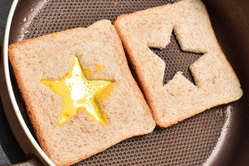 Roasting bread toasts with a star-shaped middle and omelette filled with egg to create a sandwich. Bread is fried for sandwiches in a pan with a non-stick coating, close-up