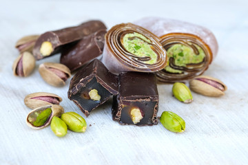 Eastern Turkish sweets with pistachios on a white wooden background. Chocolate candy with pistachios, baklava and pistachio nuts around.