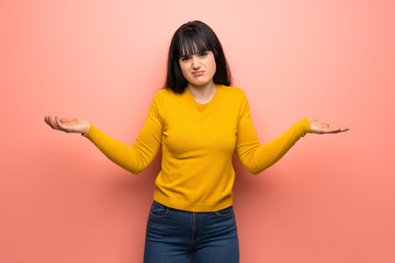 Woman with yellow sweater over pink wall unhappy because not understand something
