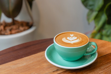 Hot cappuccino coffee in a green cup with latte art on the wooden table in the coffee shop.
