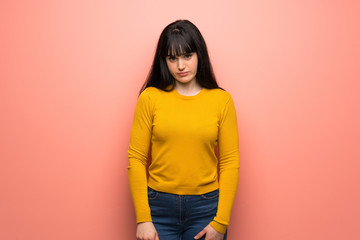 Woman with yellow sweater over pink wall with sad and depressed expression