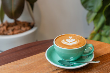 Hot cappuccino coffee in a green cup with latte art on the wooden table in the coffee shop.