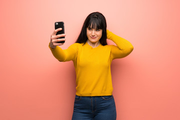 Woman with yellow sweater over pink wall making a selfie