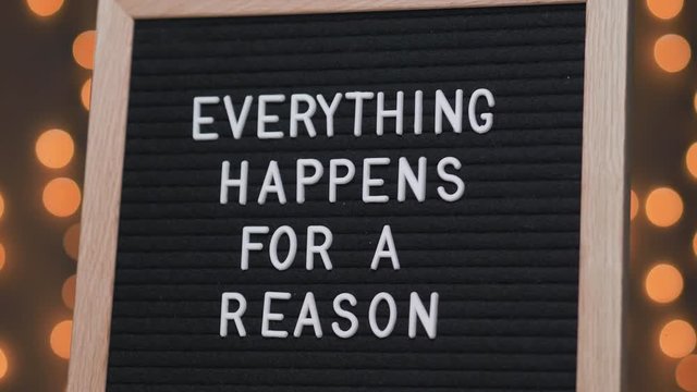 Black letter board with EVERYTHING HAPPENS FOR A REASON title on it. Camera rotating around the sign showing the beautiful bokeh balls in the background.